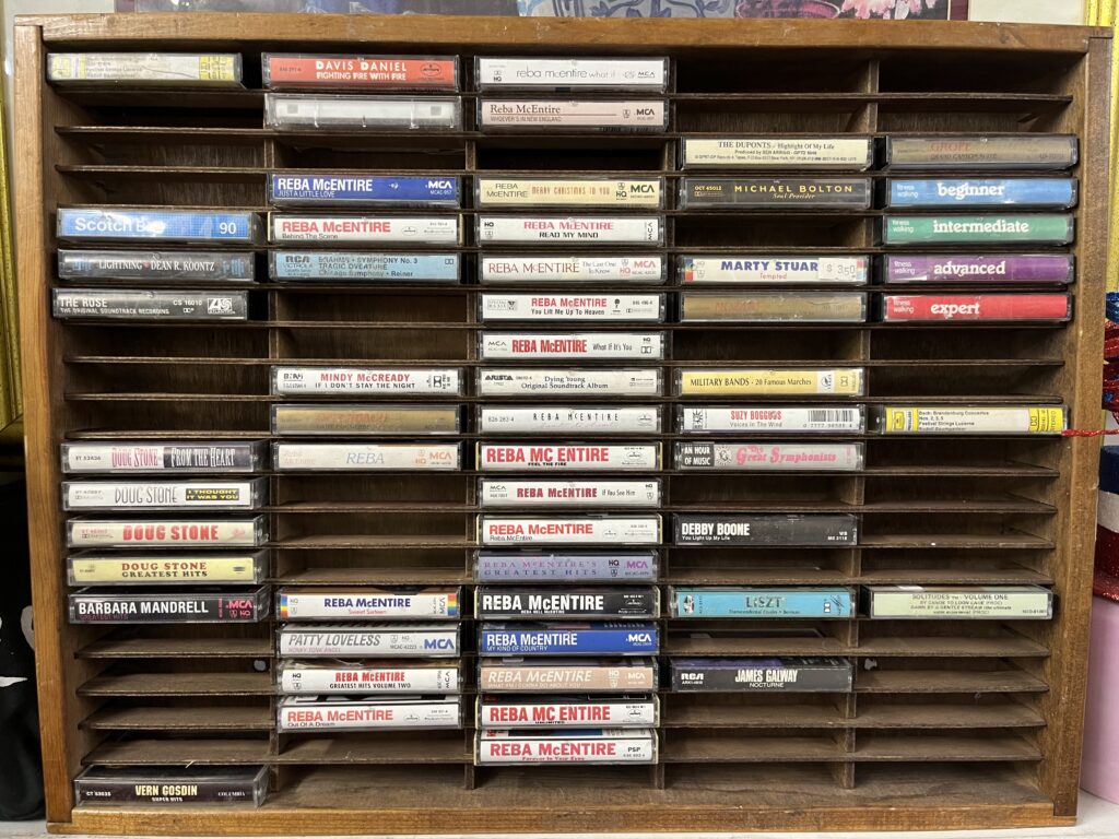 A wood cassette shelf full of used Reba McEntire tapes. 